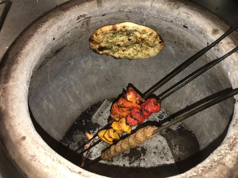 Naan and skewers cooking in the tandoor oven